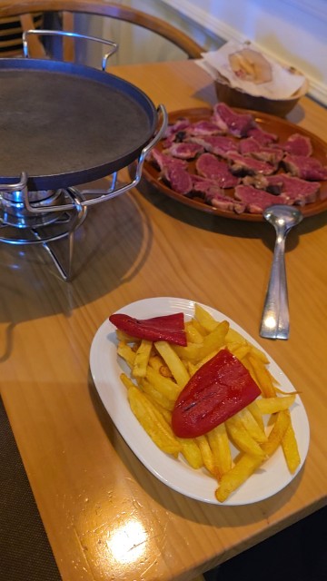a plate of french fries with peppers on top, a large plate of raw beef slices, and a hot stone