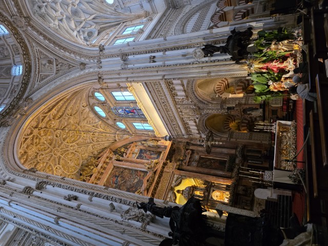 Ornate Catholic cathedral interior inside the Mezquita-Catedral in Córdoba Spain featuring elaborate gold vaulted ceilings, stained glass windows, and a decorated altar with a Christmas nativity display
