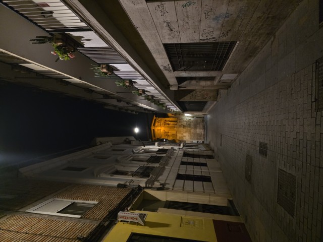 Narrow empty street in Córdoba Spain at night with flower filled balconies and a glowing historic monument visible at the end of the lane