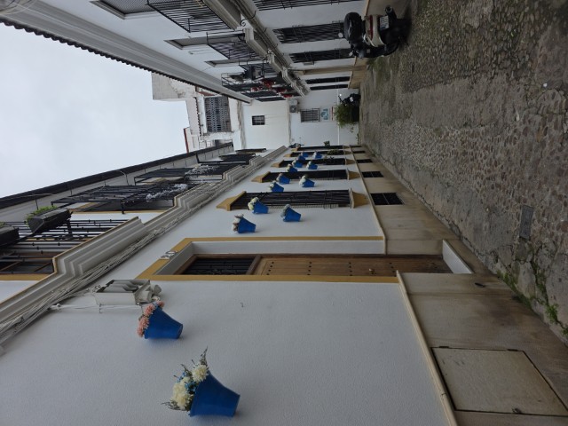 a narrow street with doors and windows with pots of plants hanging 