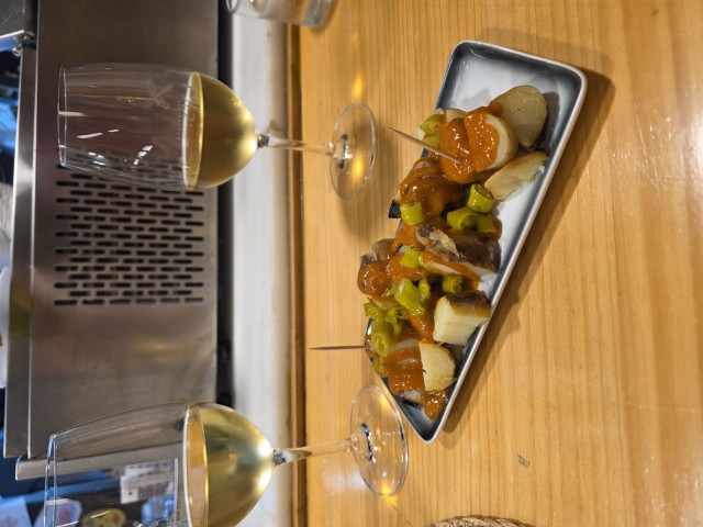 2 glasses of white wine and a metal plate with potatoes covered with a red sauce. 