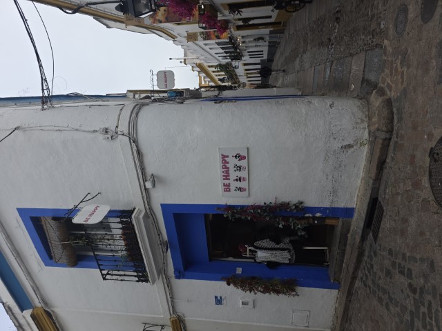 a white building with a blue window and door. There is a sign on the shop wall that says "Be Happy". Part of the Jewish Quarter in Cordoba Spain 