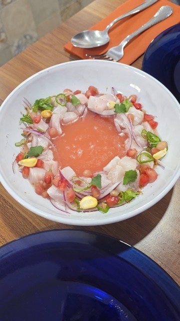 A white bowl with fish ceviche with pomegranate seeds, onions, and cilantro. 
