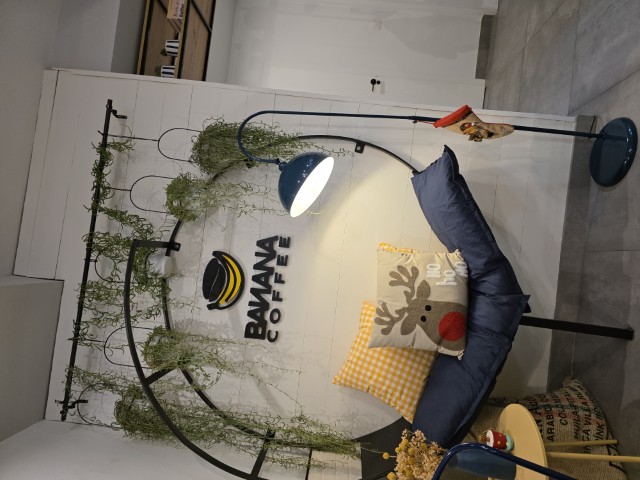 a round framed bench with plants hanging around the top. A sign displaying Banana Coffee is hanging on the wall