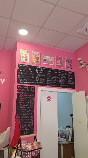 A pink wall with a black menu board with multiple options for ordering custom cakes and breads at Sensibles's Bakery in Cordoba
