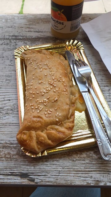 A large pastry pocket on a gold plate with a bottle of orange juice at Sensibles's Bakery in Cordoba, Spain
