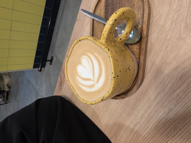 a clay, yellow mug with a latte. there is a heart design in the latte
