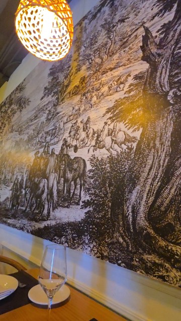 A large black and white mural with a tree and horses inside a restaurant. 