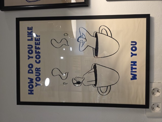 A framed poster with a man in a woman sitting in separate cups of coffee. It says "How do you like your coffee" and at the bottom it says "with you"  