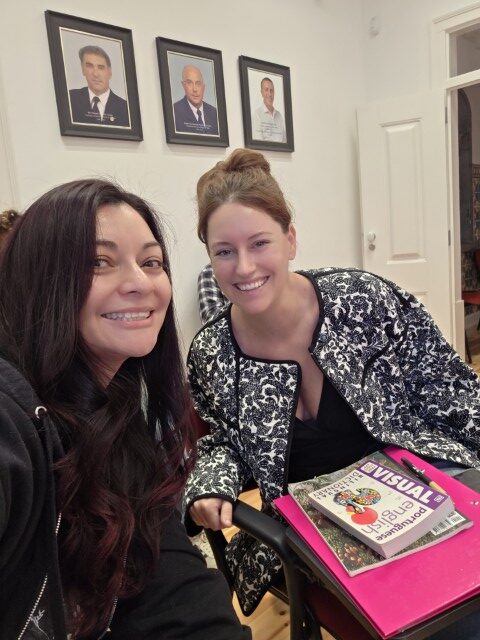 Two women smiling at a table with a European Portuguese language textbook during a language class in Portugal